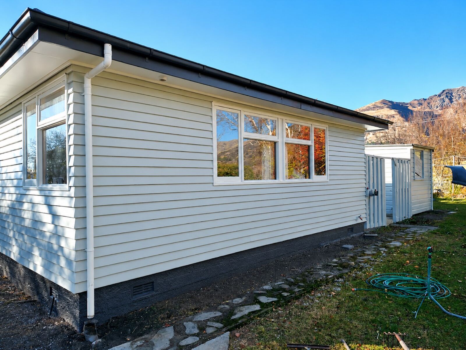 Weathered white weatherboard house before repainting, with tired paintwork and a mountain backdrop